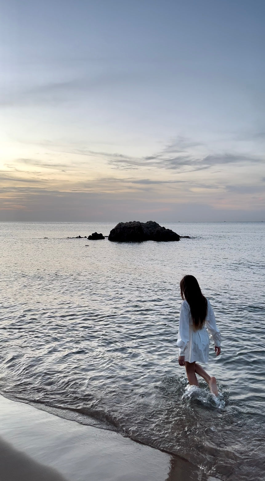une fille aux cheveux longs sur la plage en train de marcher sur le sable et l'eau. En Algérie à Mostaganem
